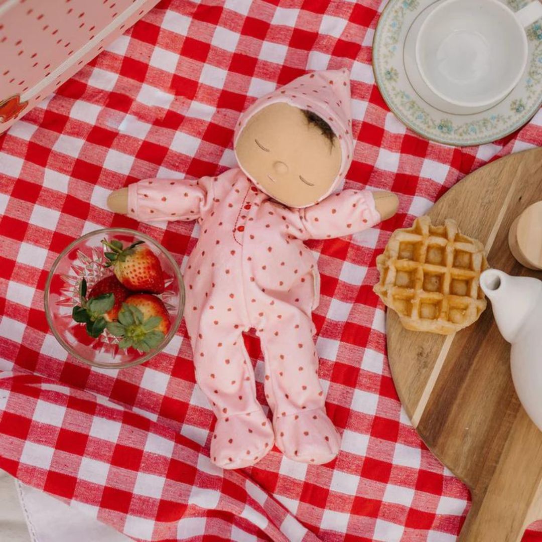 Olli Ella lappenpop Dozy Dinkum Pip op een rood-wit geruite picknickdeken met aardbeien en een wafel.