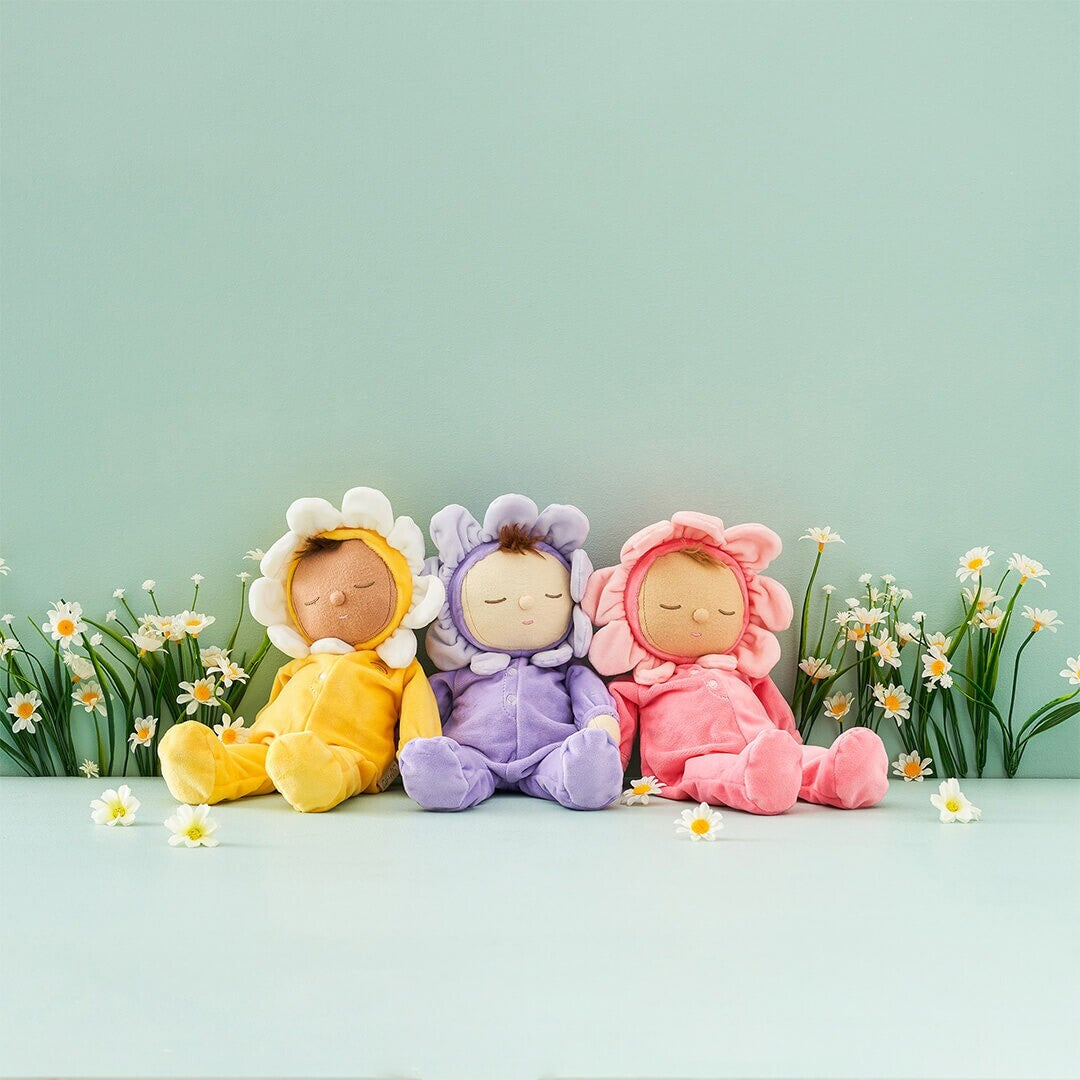 Drie Olli Ella lappenpoppen in bloemenpakjes (geel, paars, roze) zittend tussen madeliefjes.