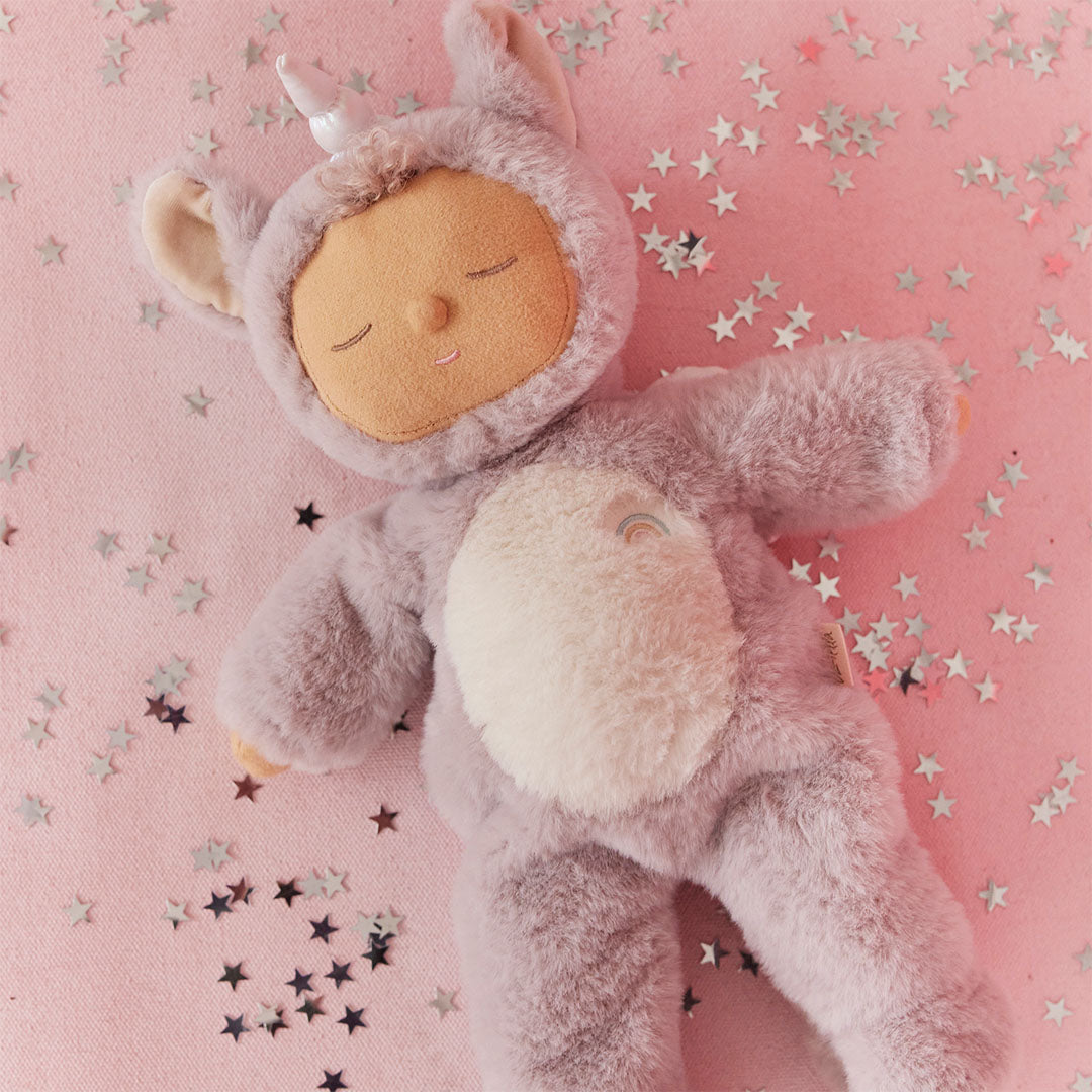 De olli ella lappenpop eenhoorn Cozy Dinkum Doll Sweetpea ligt op een roze ondergrond met zilveren sterretjes.