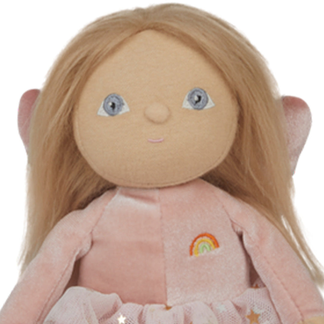 Detailopname van het gezicht van de Olli Ella lappenpop Dinky Dinkum Fairy Fiona met blonde haren, blauwe ogen en een regenboog op de borst.