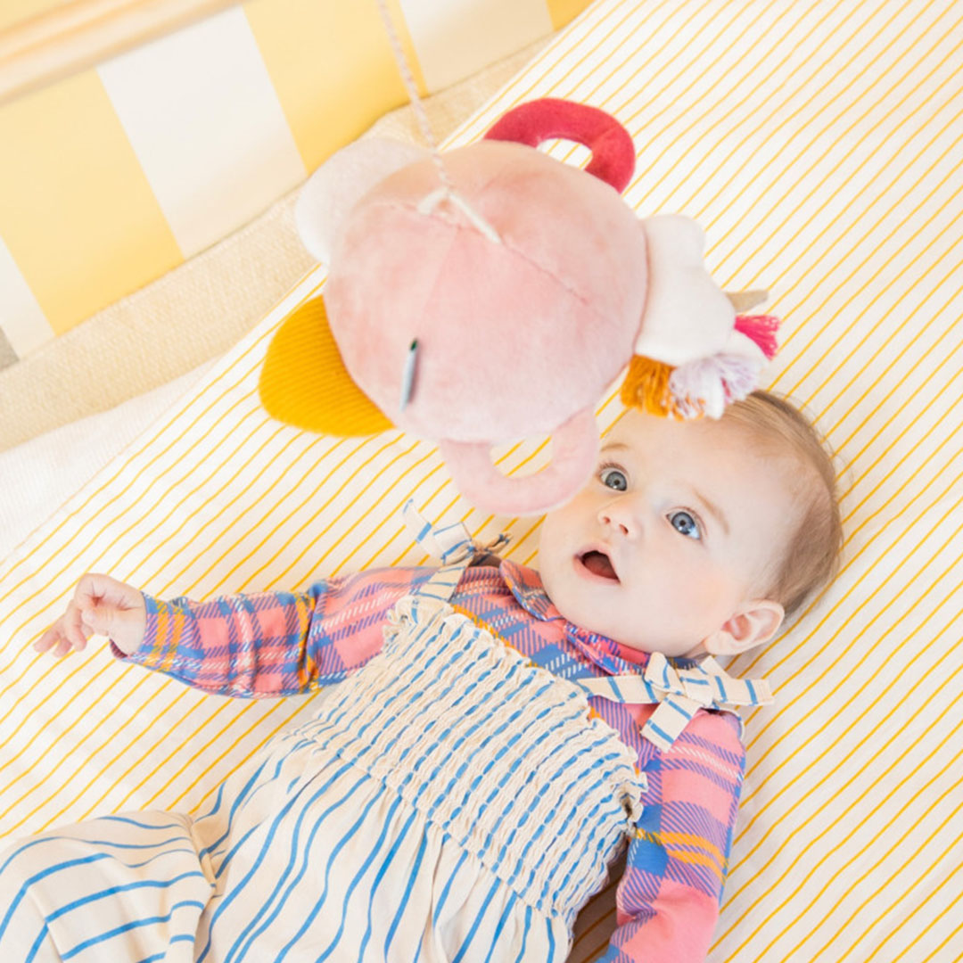 Een baby ligt op haar rug en kijkt naar de Lilliputiens activiteitenspiegel Lena de eenhoorn die boven haar hangt.