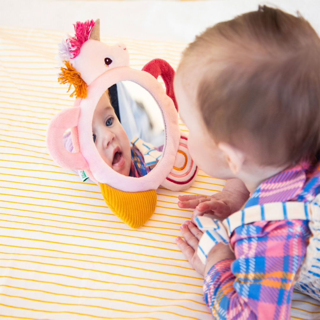 Een baby kijkt in de Lilliputiens activiteitenspiegel Lena de eenhoorn.