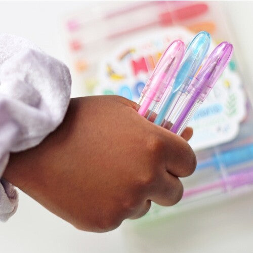 Een kinderhand houdt drie ooly geurende mini gelpennen vast in roze, blauw en paars.