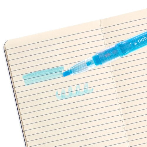 Een blauwe ooly glitter markeerstift die een streep en krabbel zet op een gelinieerd notitieboekje.