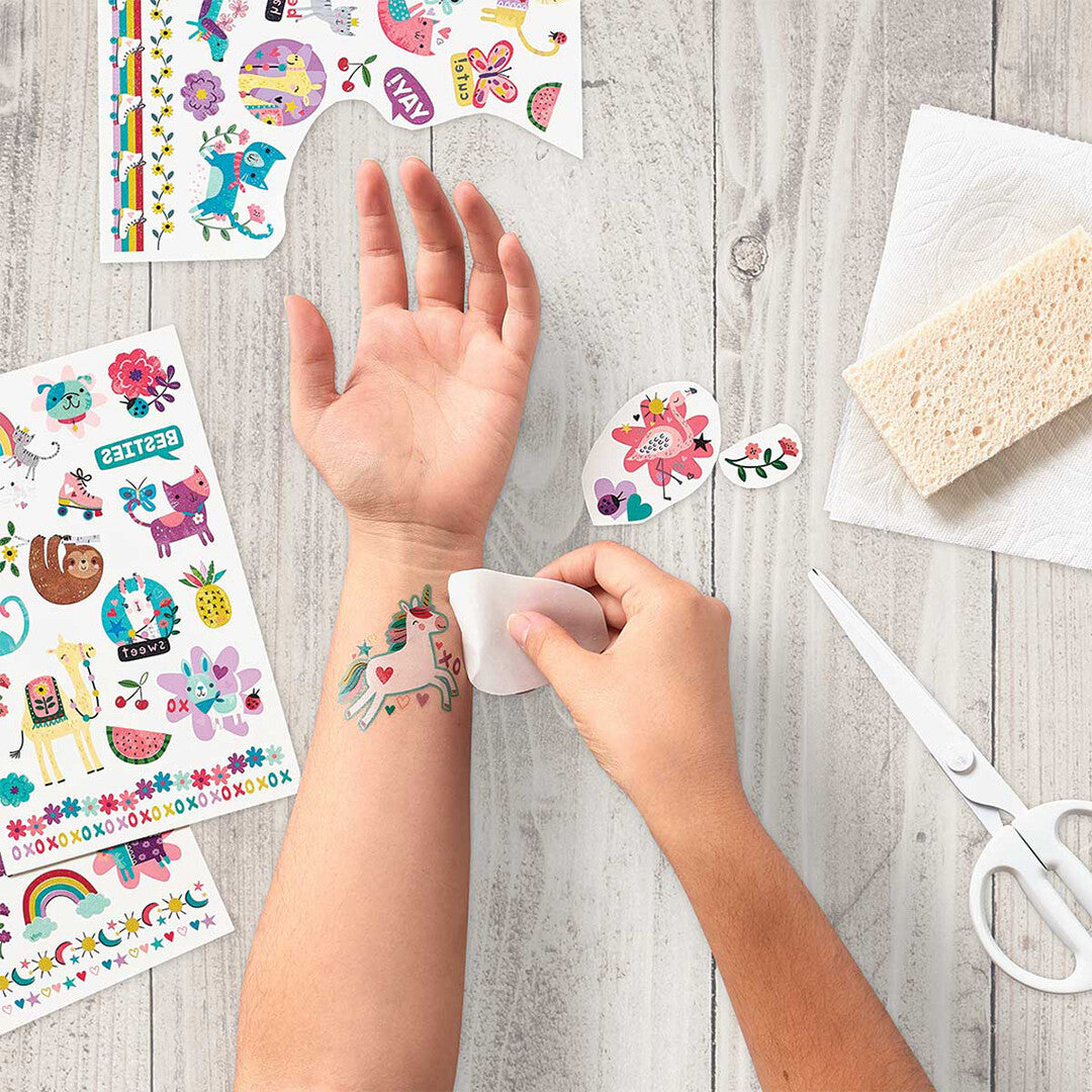Een kindertattoo van een eenhoorn wordt aangebracht op een arm, met andere Ooly tattoo-vellen ernaast.