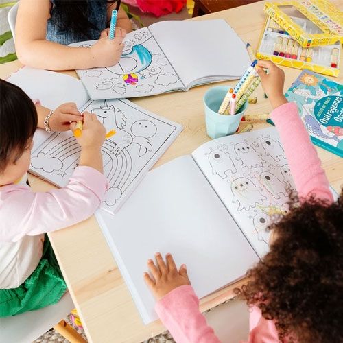 Drie kinderen kleuren aan een tafel in verschillende kleurboeken, waaronder een eenhoorn kleurboek, met kleurpotloden en stiften.