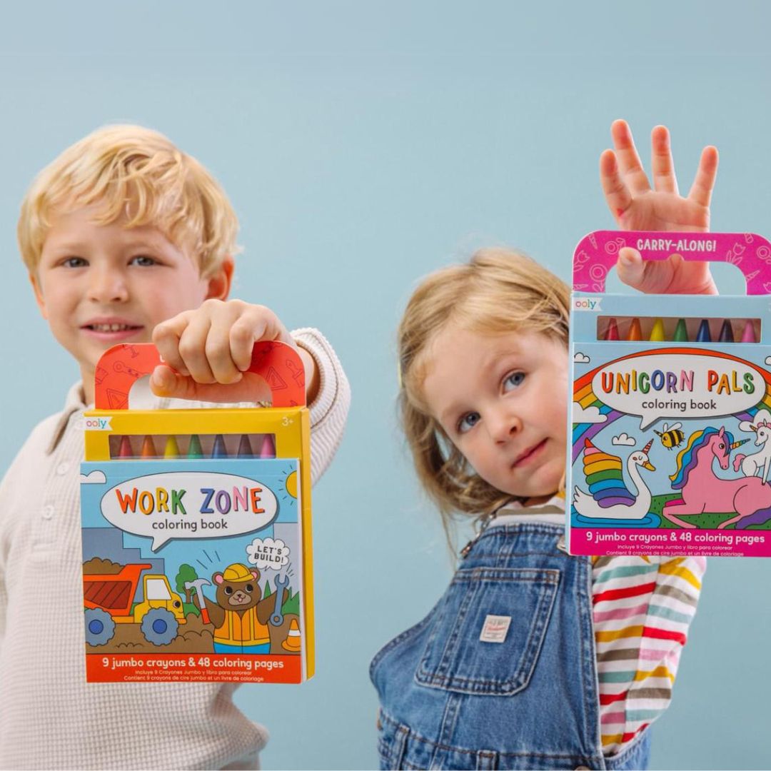 Twee kinderen houden elk een Ooly kleurboek met waskrijtjes vast, de een met een eenhoorn-thema en de ander met een bouwplaats-thema.