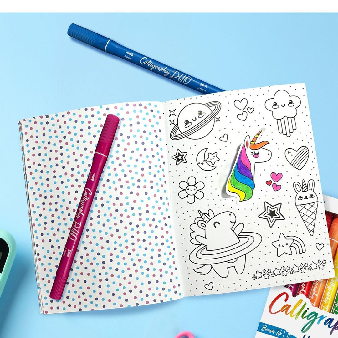 Een open pagina van het ooly stickerboek met ingekleurde en oningekleurde stickers van een eenhoorn, planeten en wolken, met twee stiften ernaast.