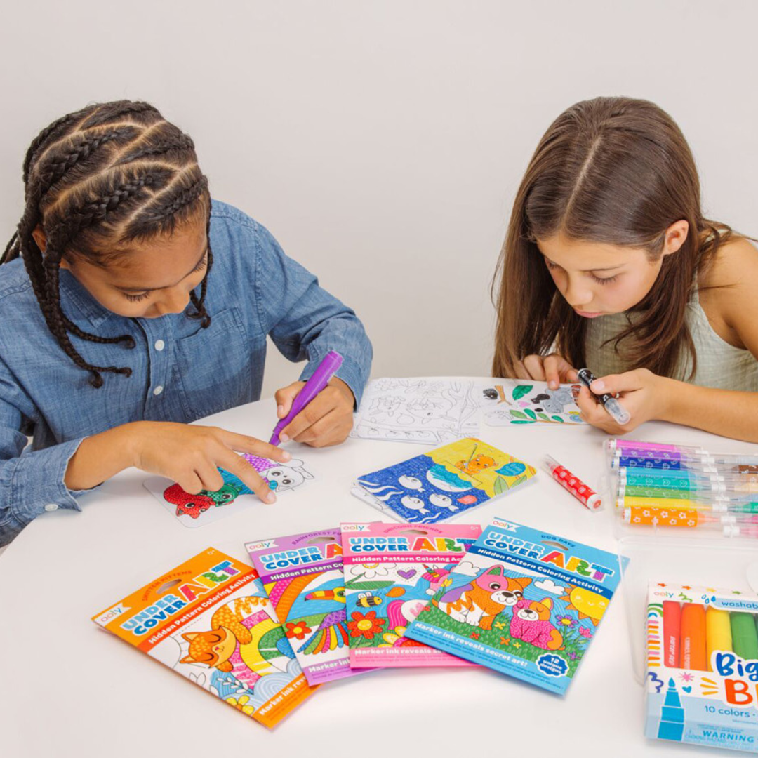 Twee kinderen kleuren aan tafel met ooly Undercover Art kleurplaten en stiften.