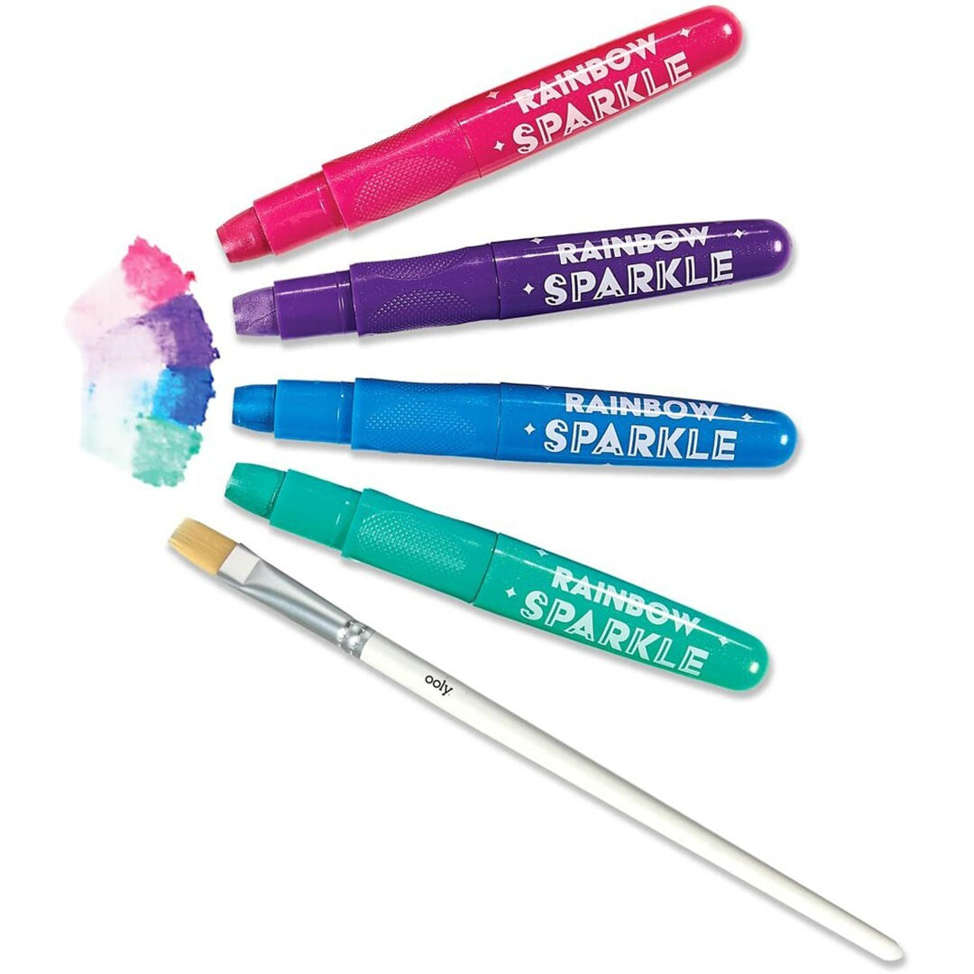 Vier ooly Rainbow Sparkle gelkrijtjes in roze, paars, blauw en groen, met een penseel en een waterverfveeg.