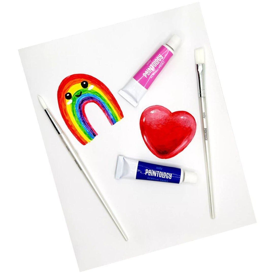 Een demonstratie van de Ooly Paintology acrylverfset met twee tubes, twee kwasten en geschilderde vormen van een regenboog en een rood hart op papier.