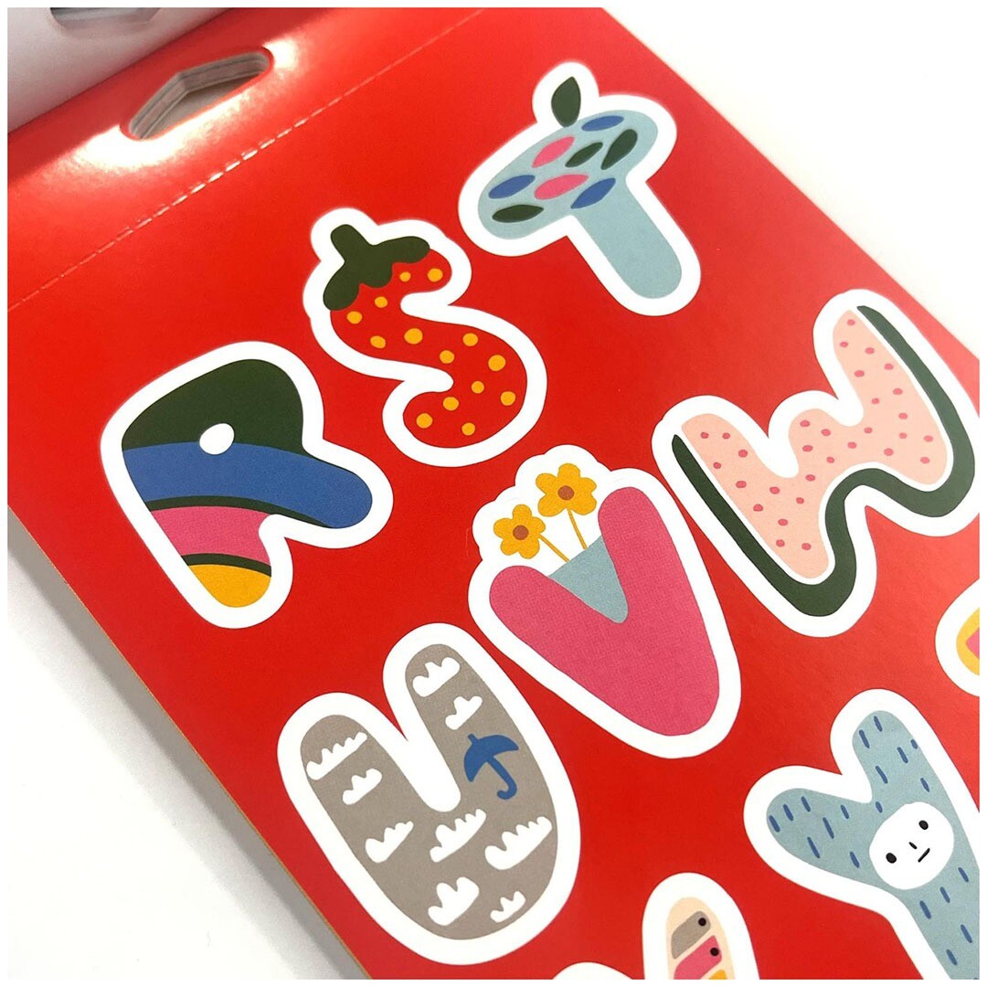 Detailopname van een rood stickerblad met kleurrijke alfabet stickers in diverse patronen.