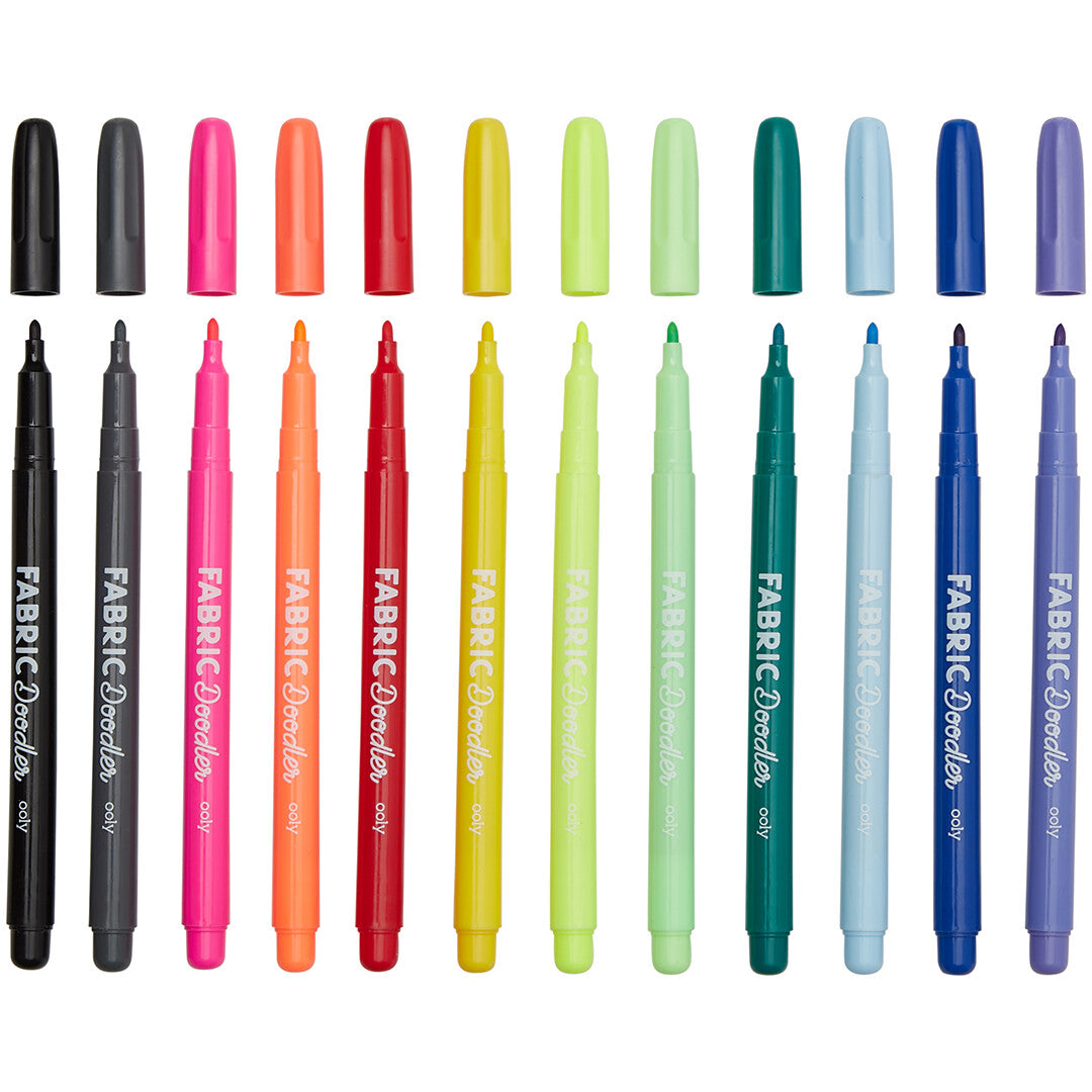 Alle 12 ooly Fabric Doodlers textielstiften in regenboogkleuren, met de doppen ernaast.