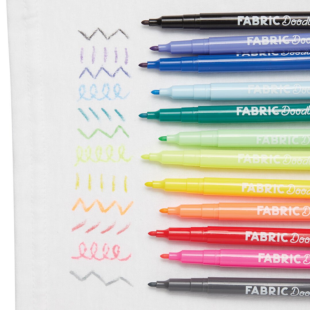 ooly Fabric Doodlers textielstiften die verschillende gekleurde lijnen en patronen tekenen op witte stof.