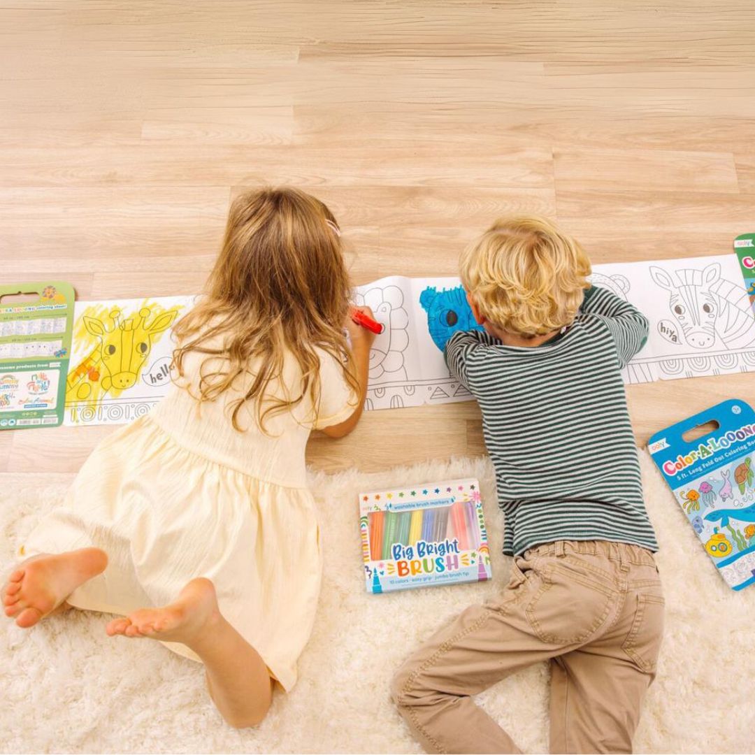 Twee kinderen liggen op de grond en kleuren samen een lang uitgevouwen ooly kleurboek met zeedieren.