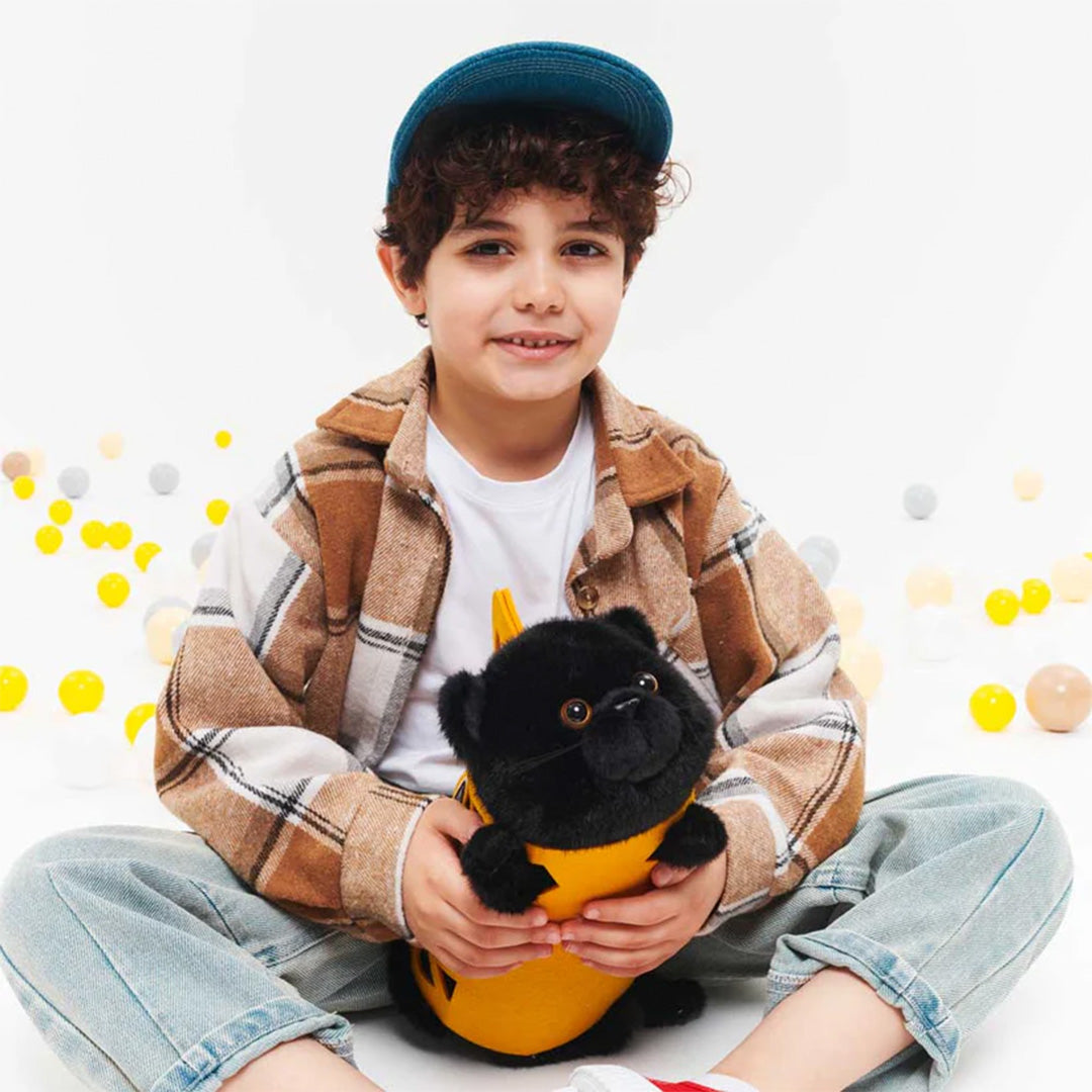 Een jongen zit met de Orange Toys pluchen zwarte kat Milo in de gele draagtas op schoot.
