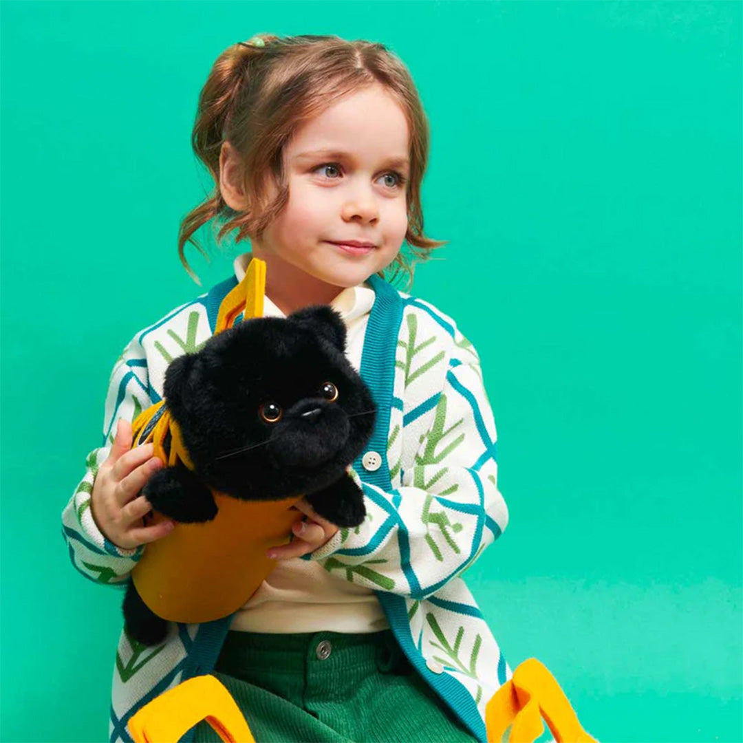 Een jong meisje houdt de Orange Toys pluchen zwarte kat Milo in de gele draagtas vast.