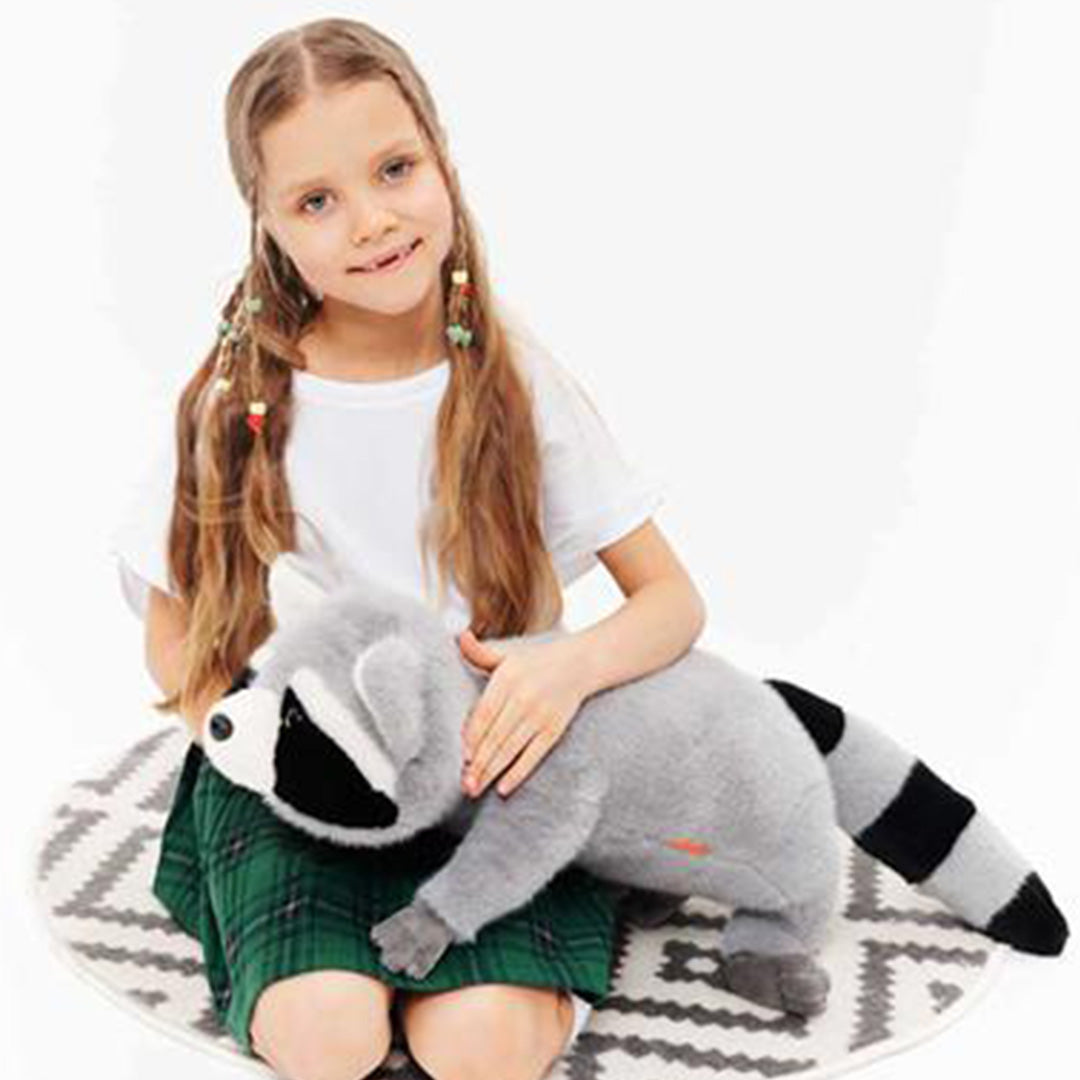 Een meisje zit op een kleed en aait de pluchen wasbeer.