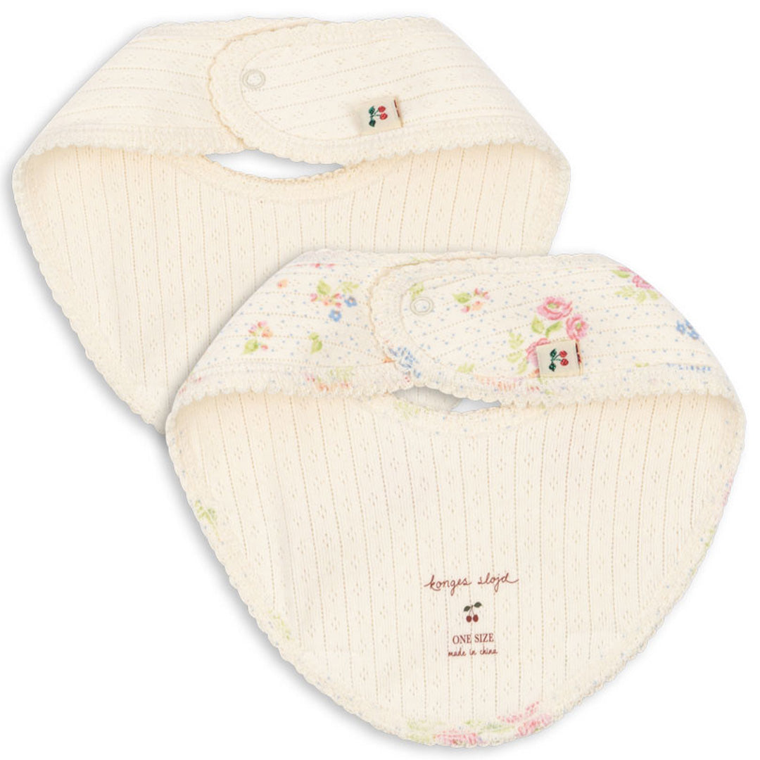 Twee Konges Sløjd babyslabjes, één effen beige en één beige met bloemenpatroon, met merklabel zichtbaar.