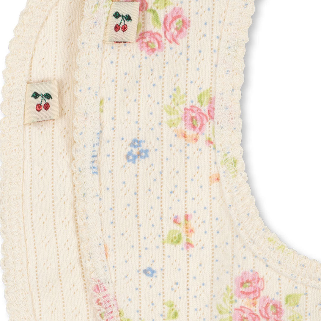 Detailopname van de Konges Sløjd babyslabjes met gebreide textuur, bloemenpatroon en kersenlabels.