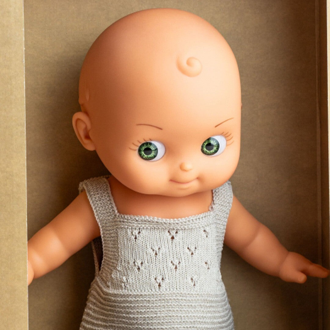 Close-up van de Paola Reina babypop Mini Pancha met groene ogen en grijze gebreide outfit.