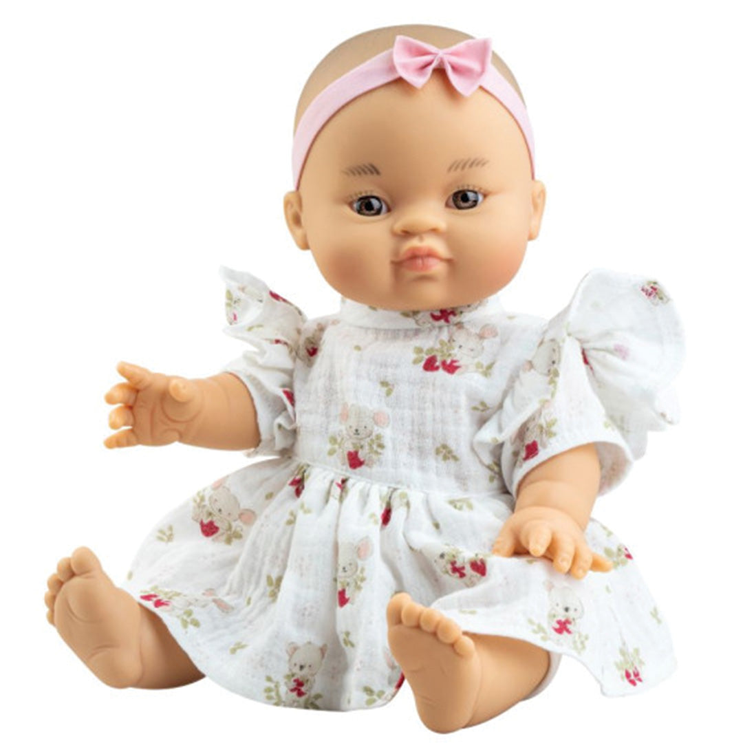 Paola Reina babypop Alessandra zit met een witte jurk met dierenprint en een roze haarband.