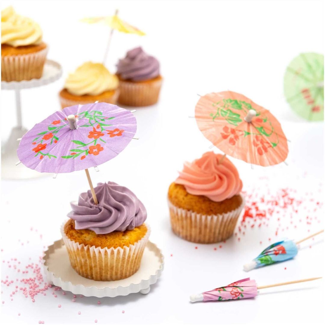 Rico Design cocktailparaplu's met gebloemd patroon steken in cupcakes met gekleurde frosting.