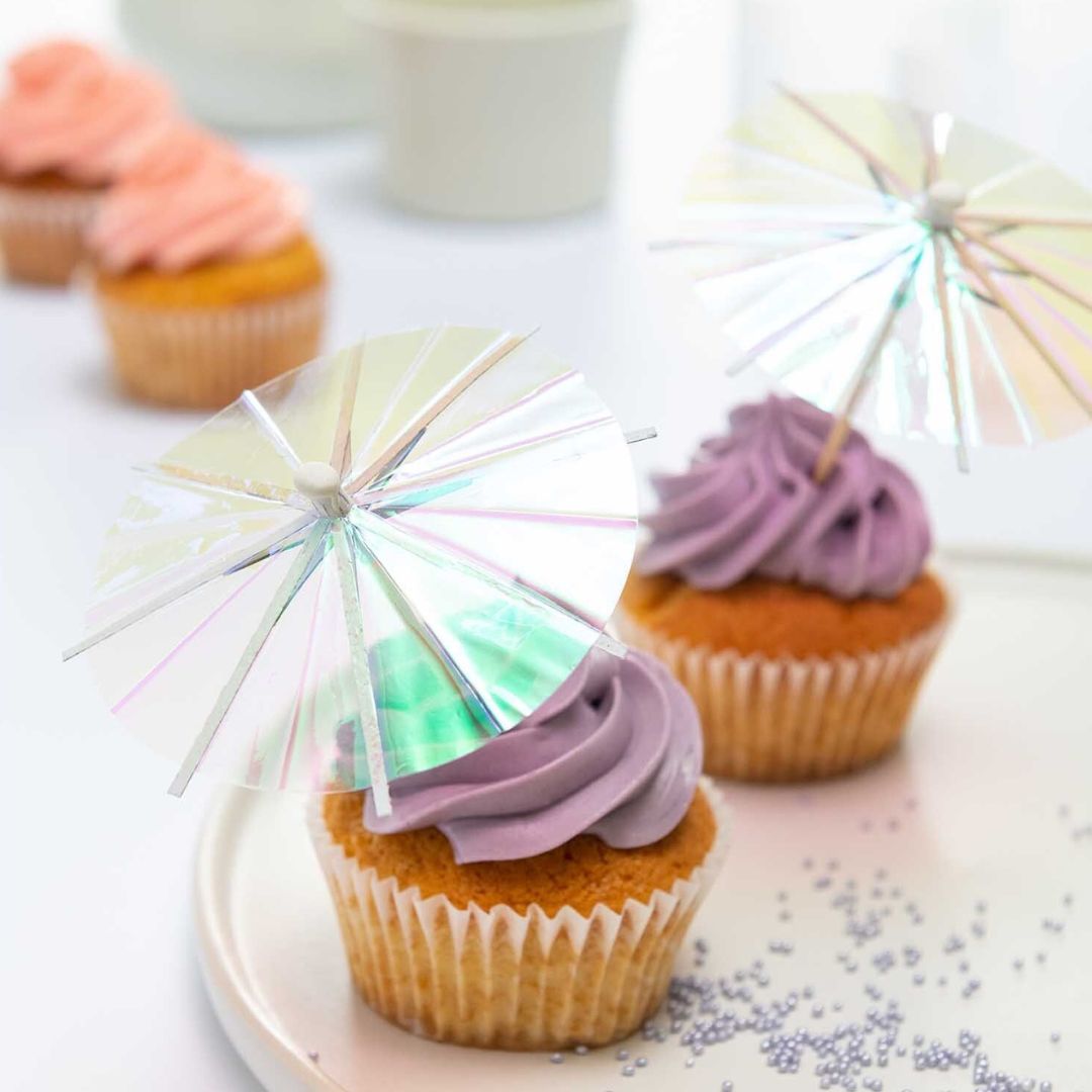 Twee cupcakes met paarse frosting en holografische Rico Design cocktailparaplu's.
