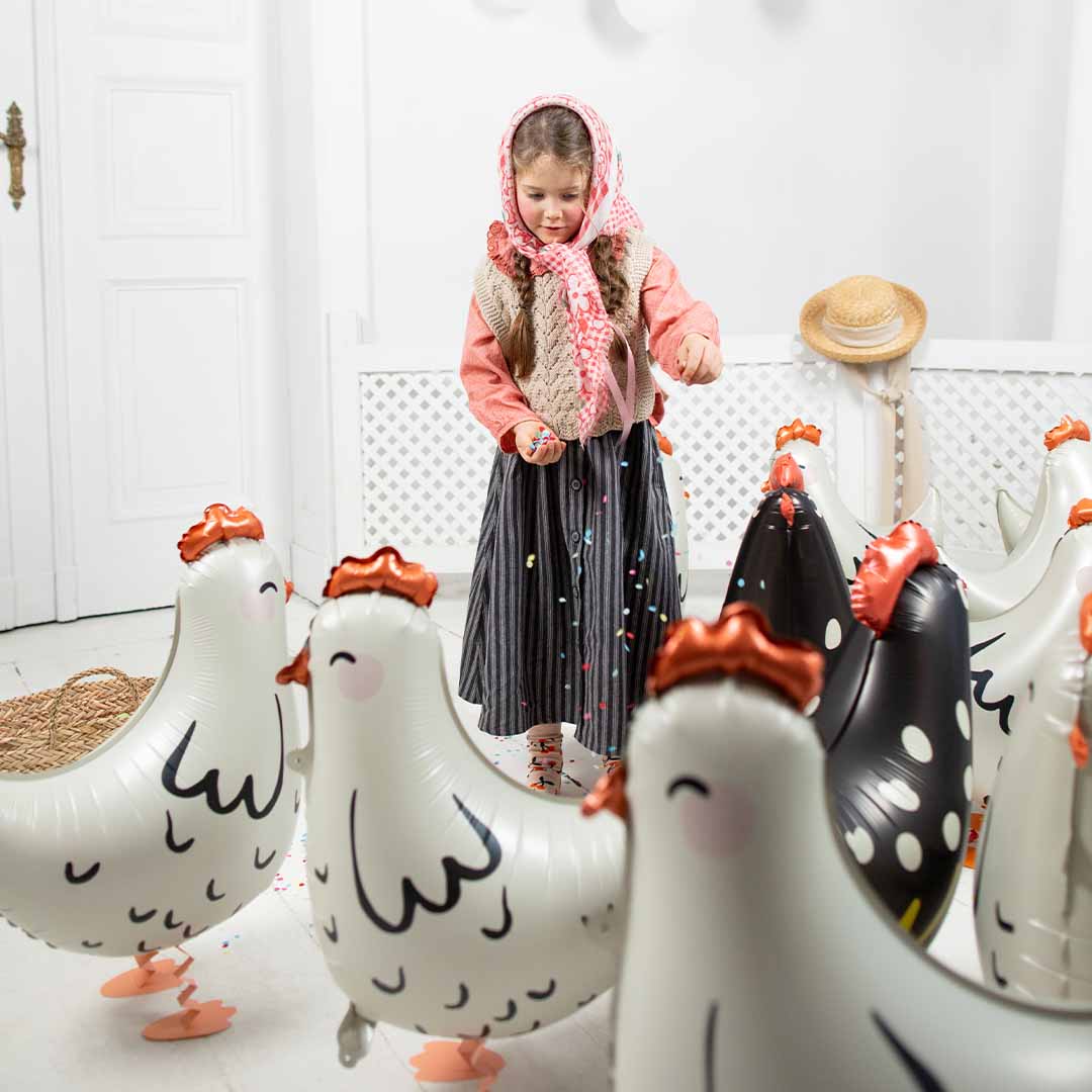 Een meisje strooit confetti tussen meerdere Partydeco folieballonnen in de vorm van kippen.