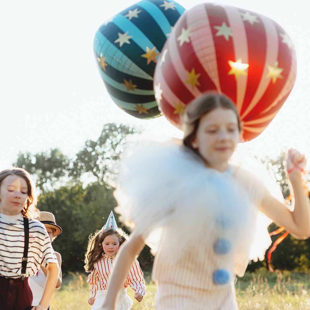 Kinderen rennen door een veld met een rode en blauwe gestreepte folieballon.