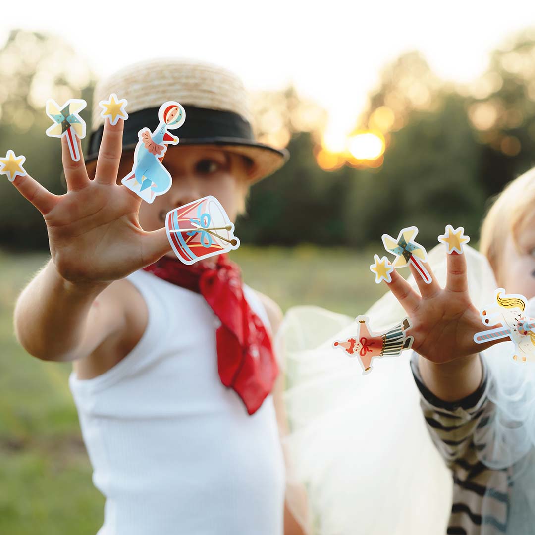 Twee kinderen met partydeco circus stickers op hun vingers, met een zonsondergang op de achtergrond.