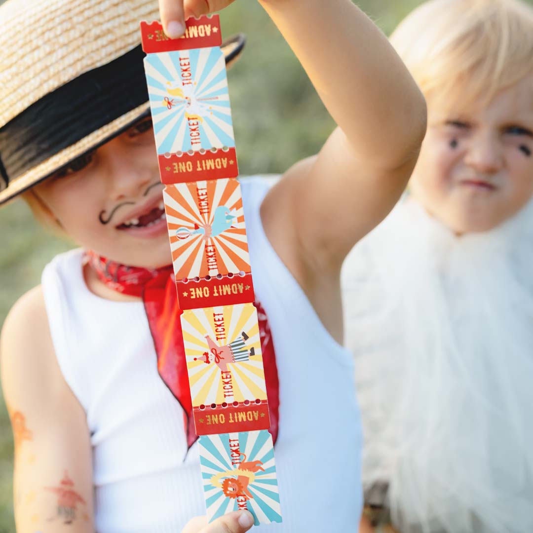 Een kind houdt een strook partydeco circus entreekaartjes omhoog, met een ander kind op de achtergrond.