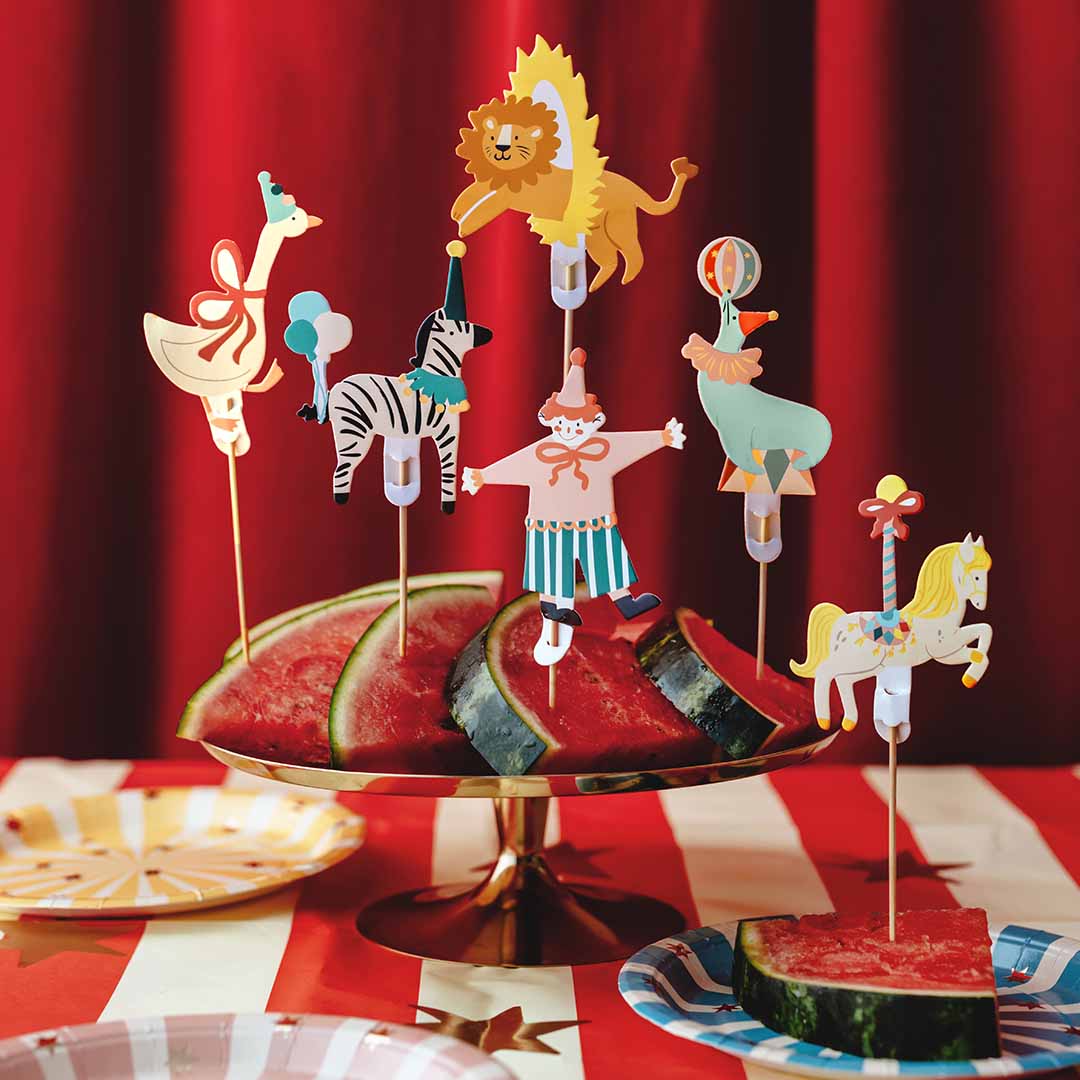 Partydeco circus taartversiering prikkers gestoken in watermeloen op een feestelijk gedekte tafel.