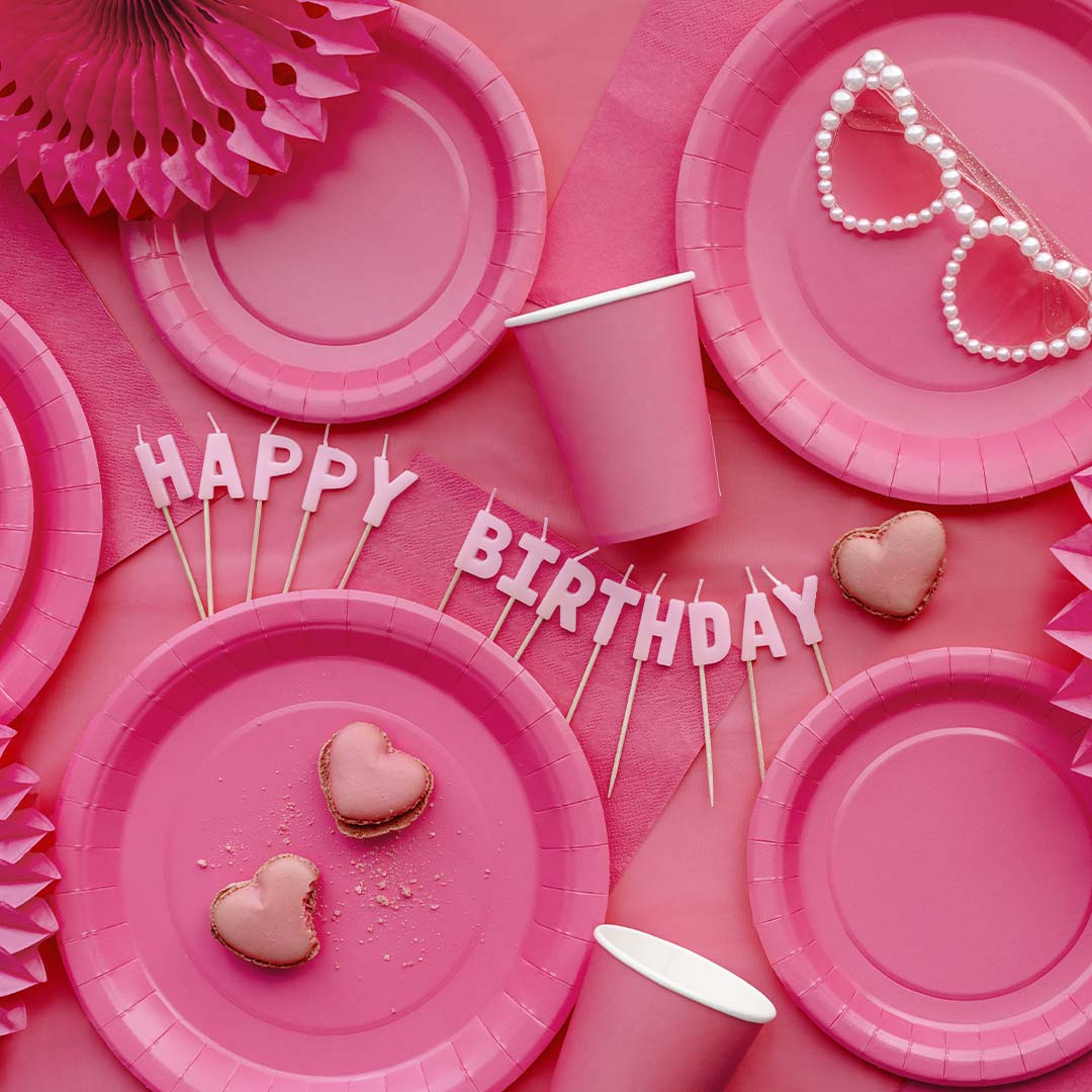 Een collectie roze feestartikelen met borden, bekers en 'Happy Birthday' kaarsen.