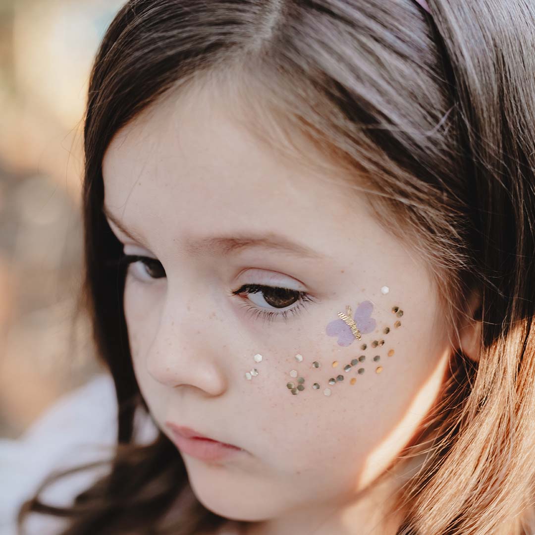 Detail van een kindergezicht met een tijdelijke vlindertatoeage en glitter op de wang.