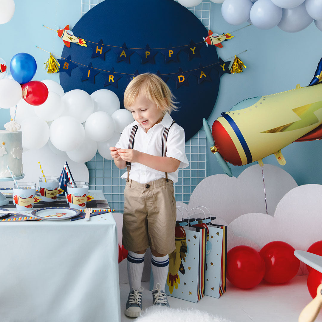 Een jongen viert zijn verjaardag aan een feestelijk gedekte tafel met vliegtuigthema decoraties.