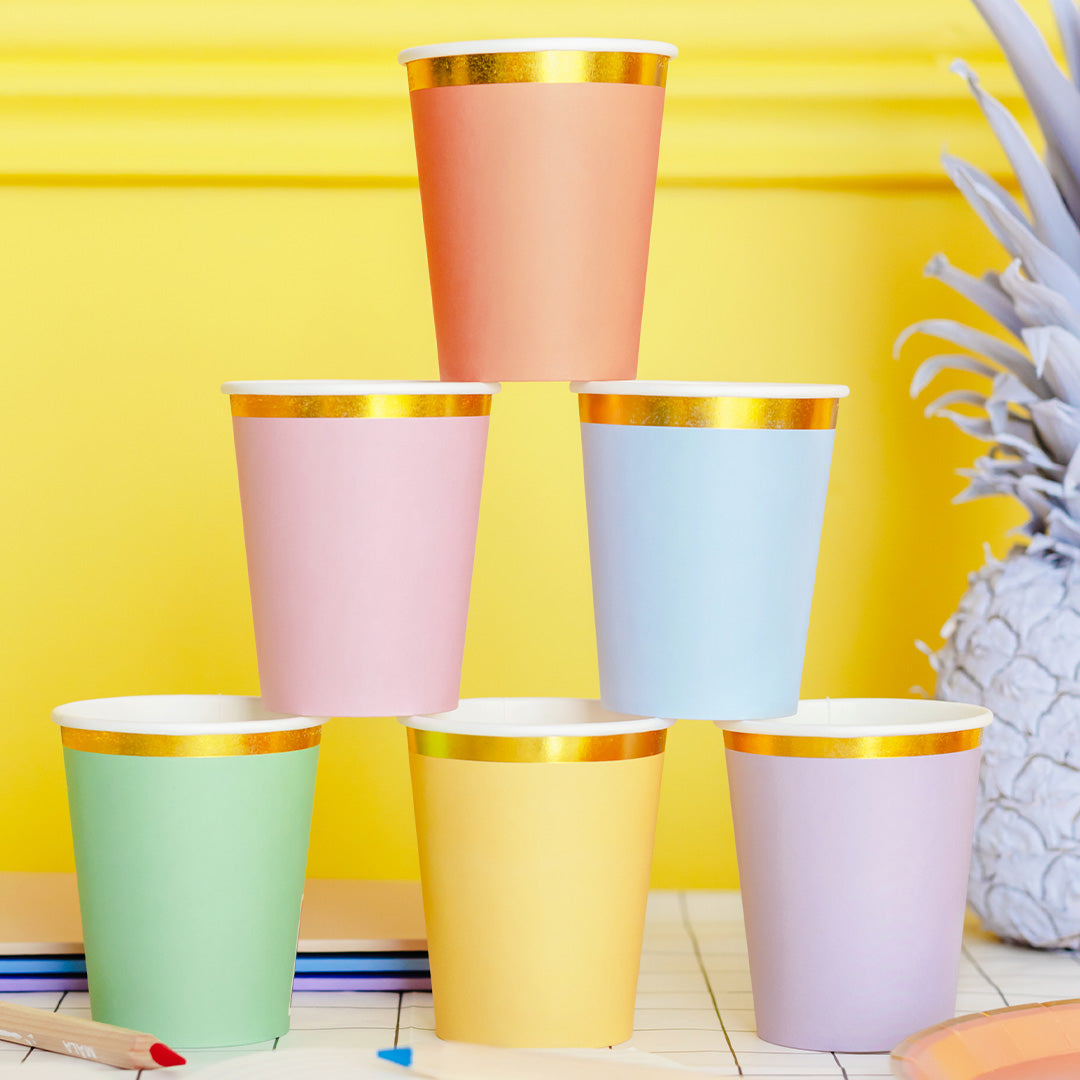 Een piramide van zes partydeco pastelkleurige papieren bekers met gouden rand op een gele achtergrond.