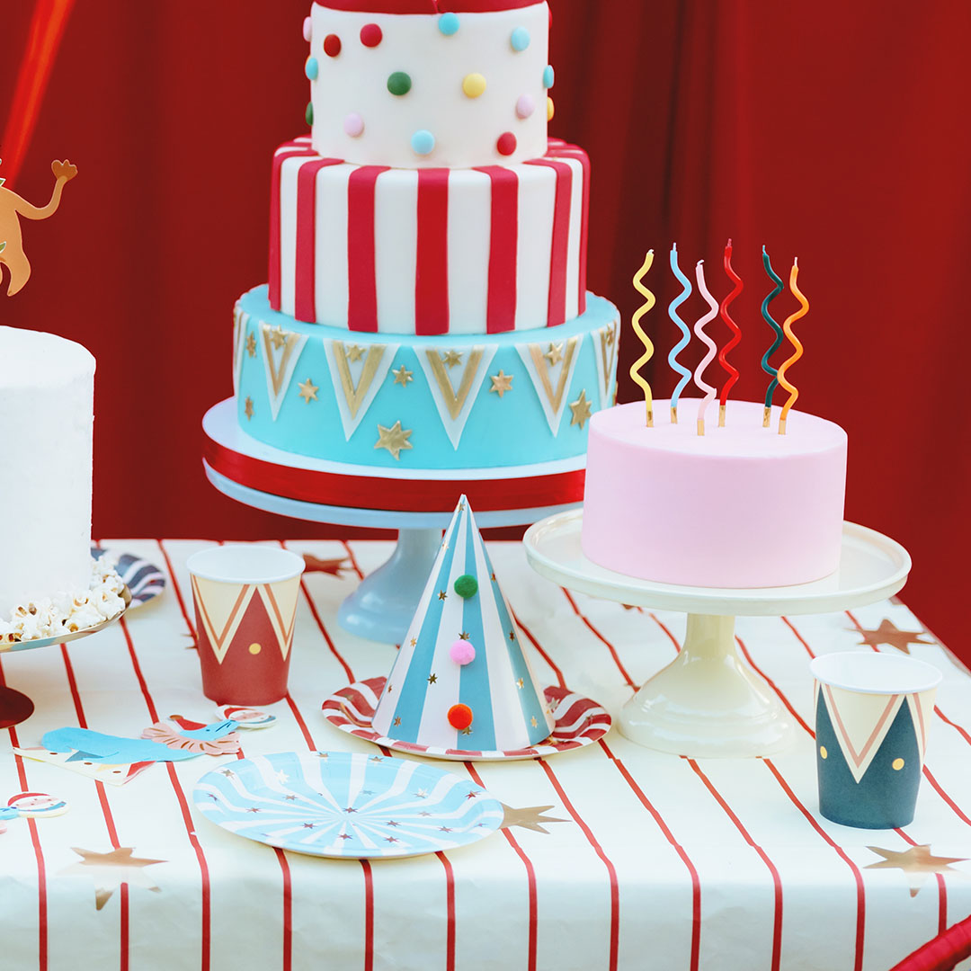 Een feesttafel met twee taarten, een feesthoed en twee partydeco feestbekers met circuspatroon.