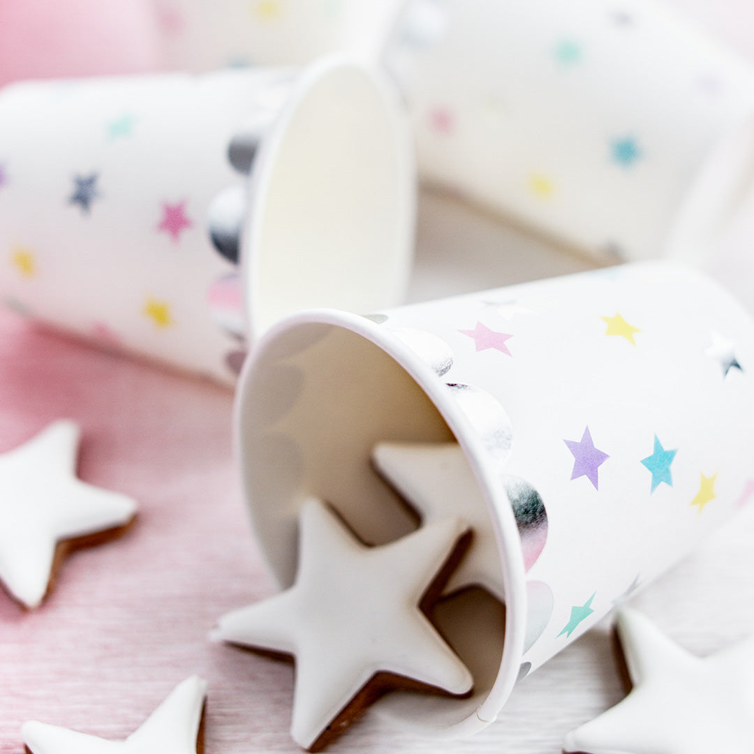 Partydeco papieren bekers met sterrenpatroon, waarvan één gevuld is met sterkoekjes op een roze ondergrond.