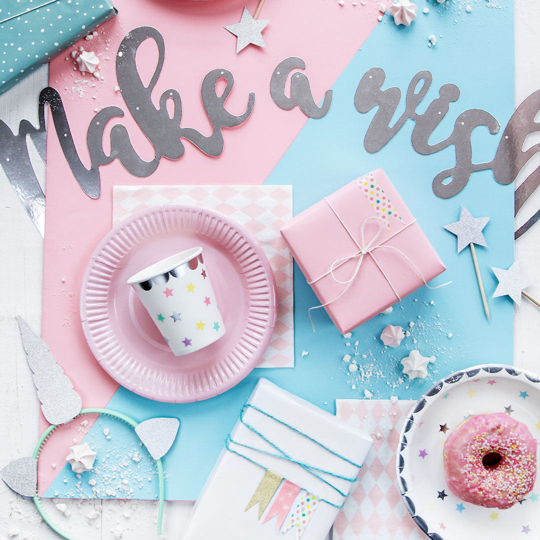 Partydeco papieren beker met sterrenpatroon op een roze bord, omringd door verjaardagsdecoraties en cadeaus.