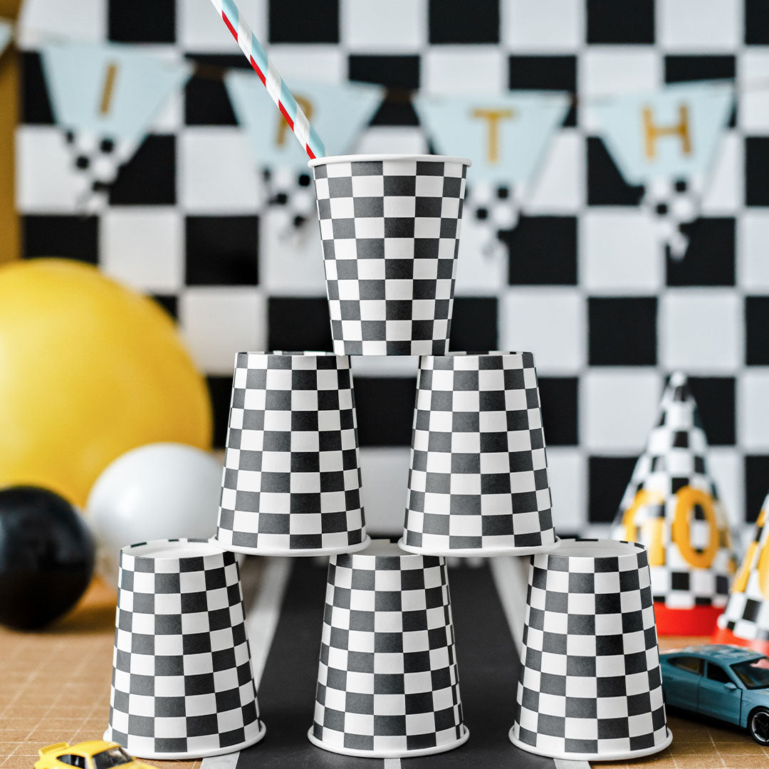 Een piramide van partydeco papieren bekers met een zwart-wit geruit patroon op een tafel met racebaan-decoratie.