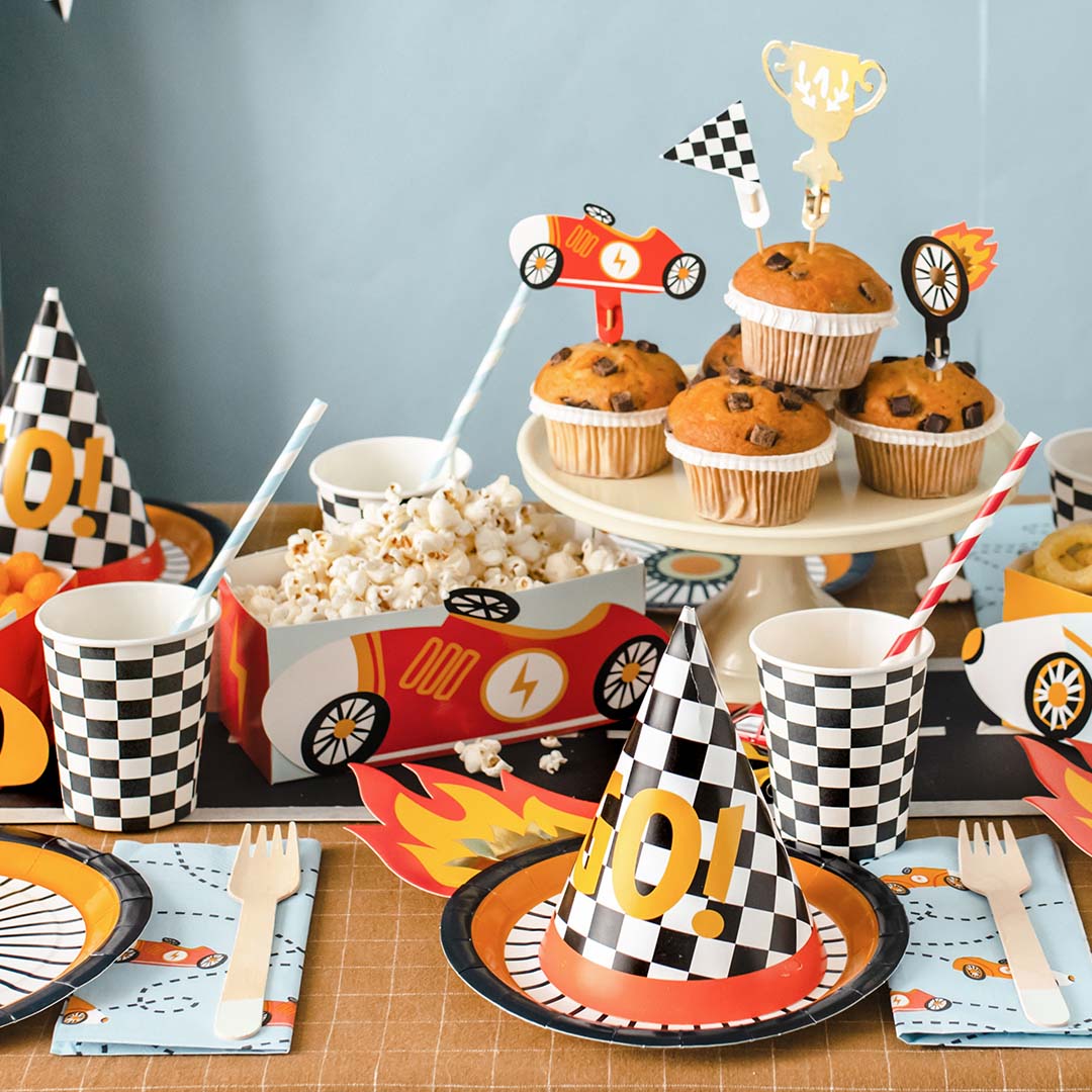 Een feestelijk gedekte tafel met partydeco papieren bekers, borden en feesthoedjes met een raceauto en geruit patroon.