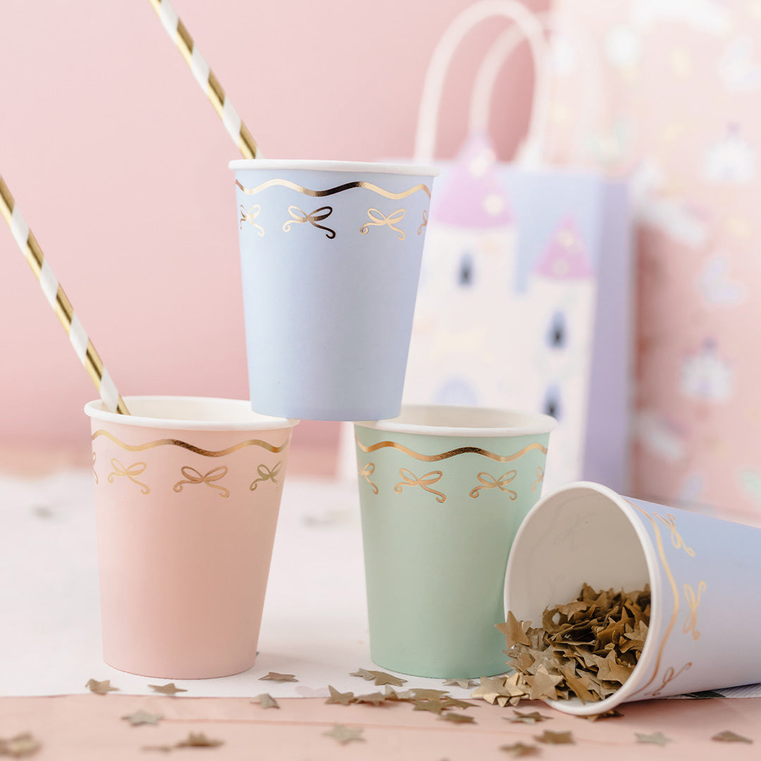 Partydeco papieren feestbekers met strikjes, gevuld met gouden sterconfetti en rietjes, op een feestelijke achtergrond.