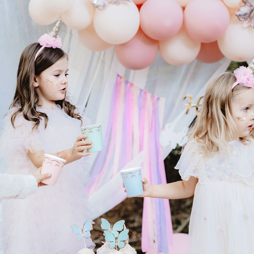Twee meisjes op een feestje drinken uit Partydeco papieren bekers met strikjes.
