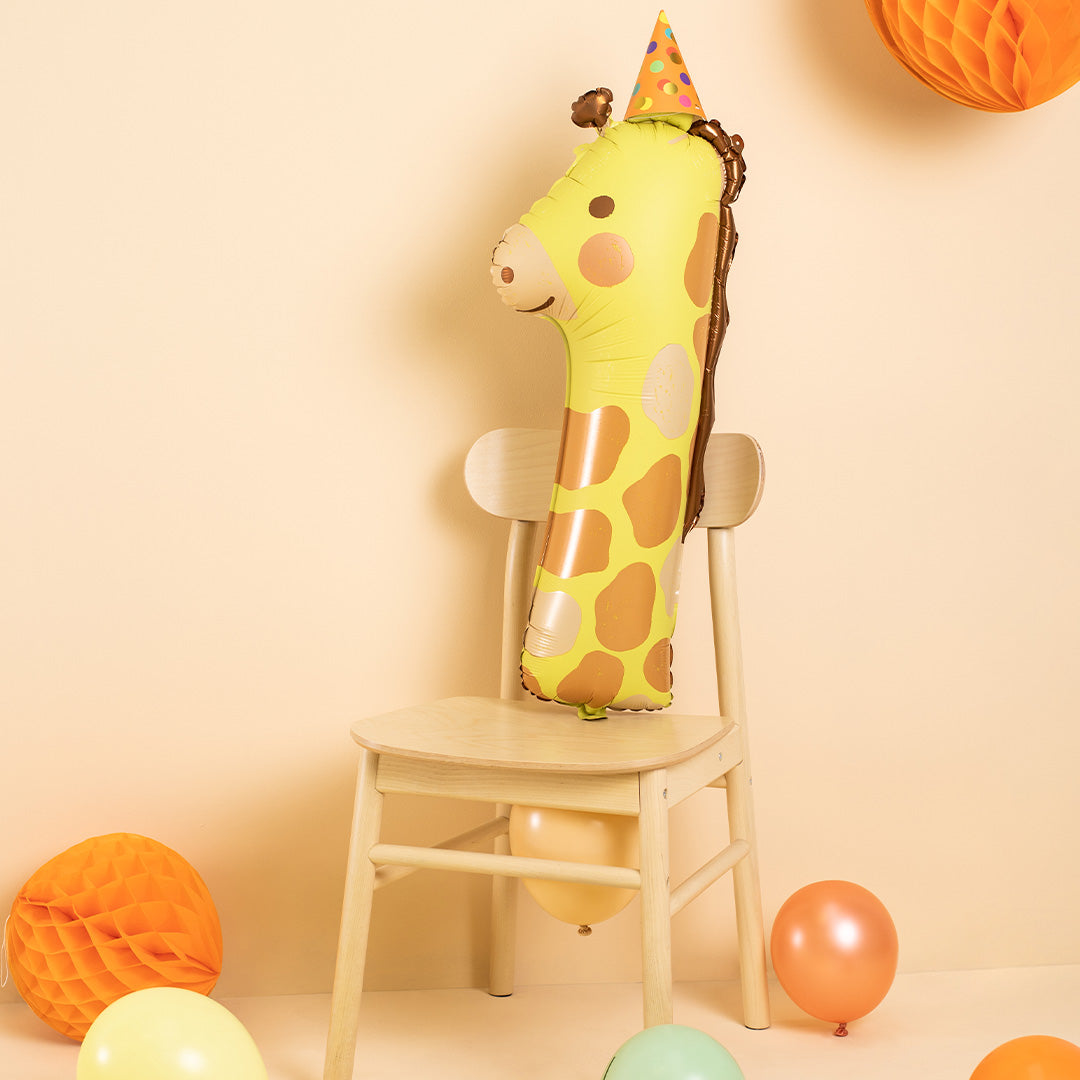Partydeco cijferballon 1 in de vorm van een giraf met feesthoedje, staand op een houten stoel tussen andere feestdecoraties.