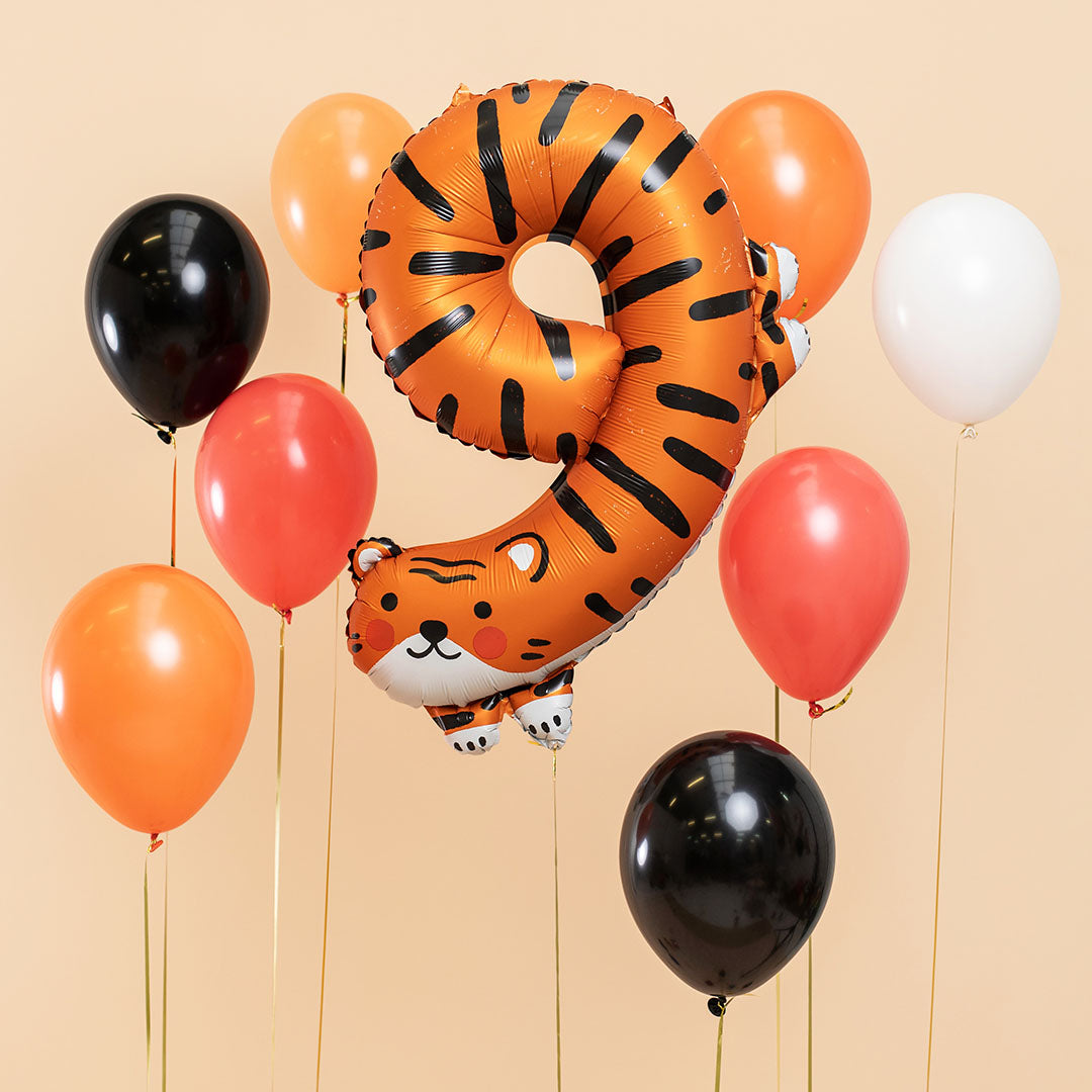 Partydeco cijferballon 9 in tijgerthema, zwevend tussen zwarte, oranje, rode en witte ballonnen.