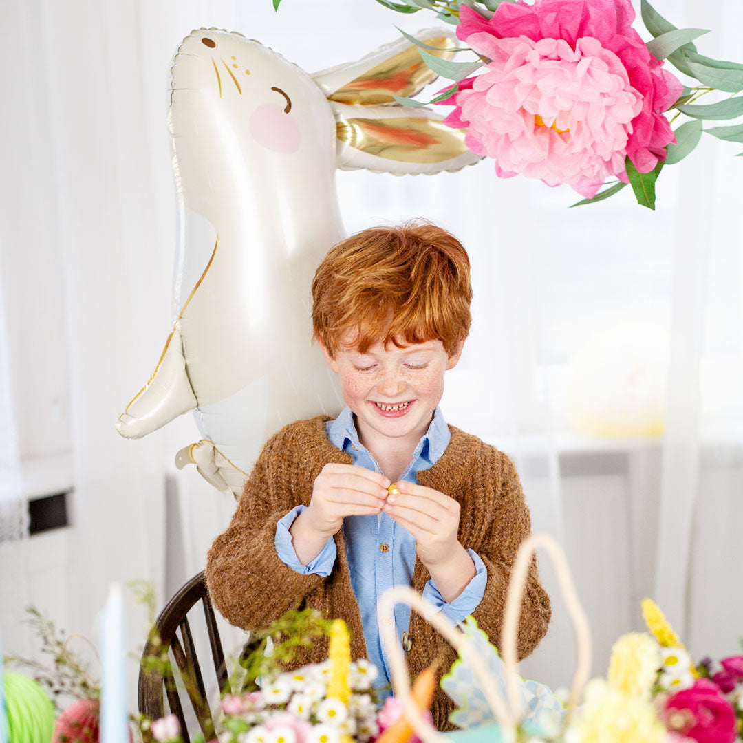 Een lachende jongen zit aan tafel met de witte haas folieballon op de achtergrond.
