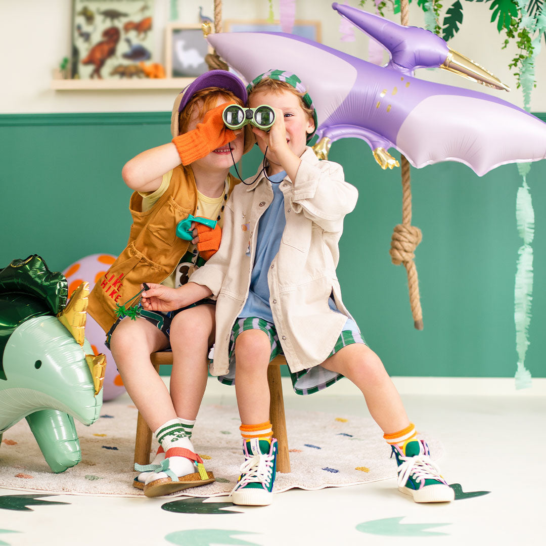 Twee jongens spelen met verrekijkers op een dinosaurusfeestje met een Partydeco pterodactyl folieballon.