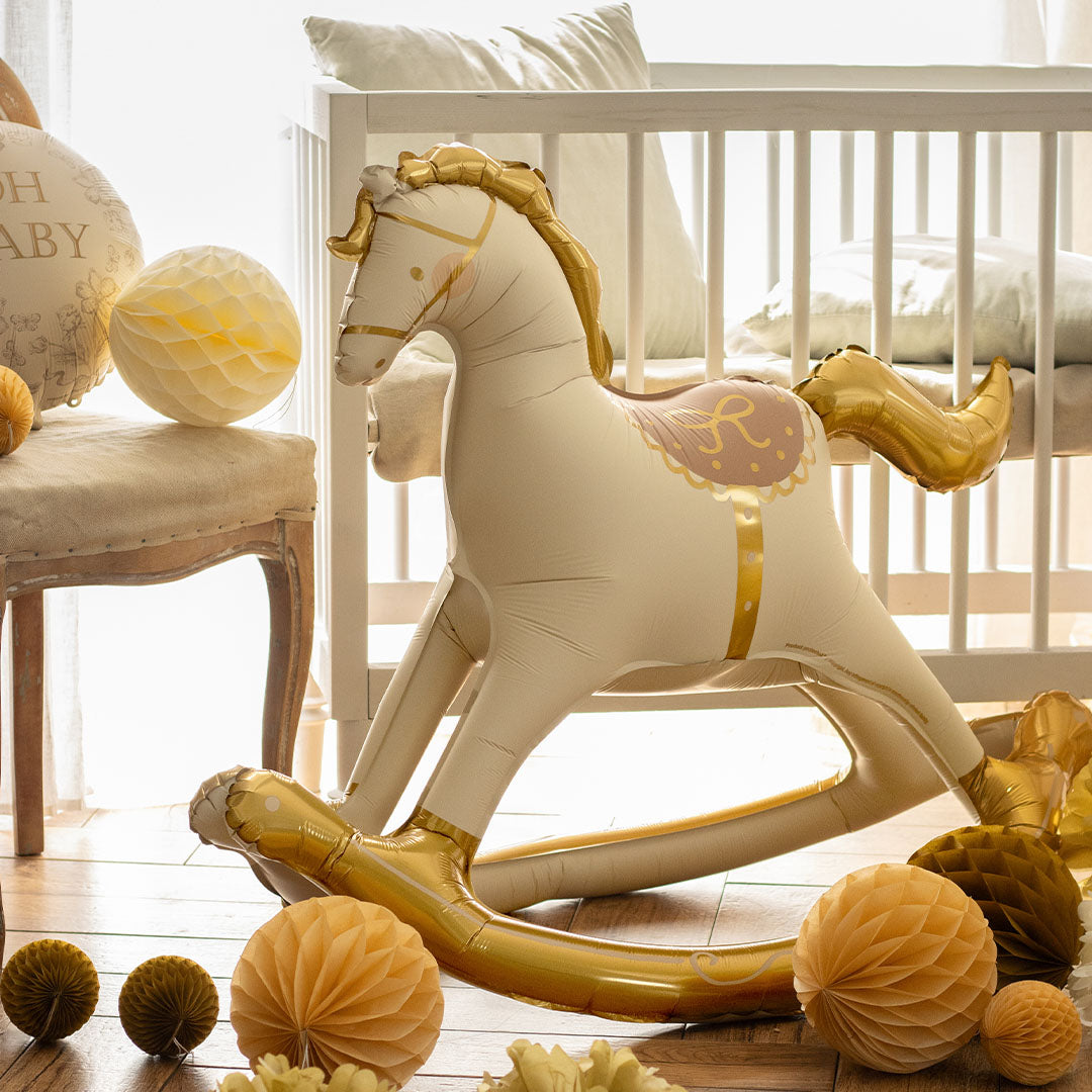 partydeco folieballon schommelpaard in een babykamer met een wieg en andere feestdecoraties.