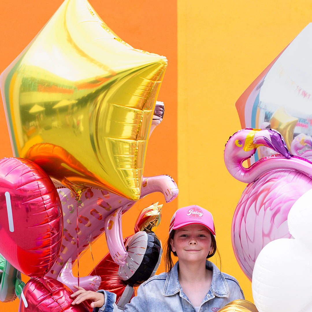 Meisje met roze pet naast een partydeco gouden ster folieballon en andere feestballonnen.